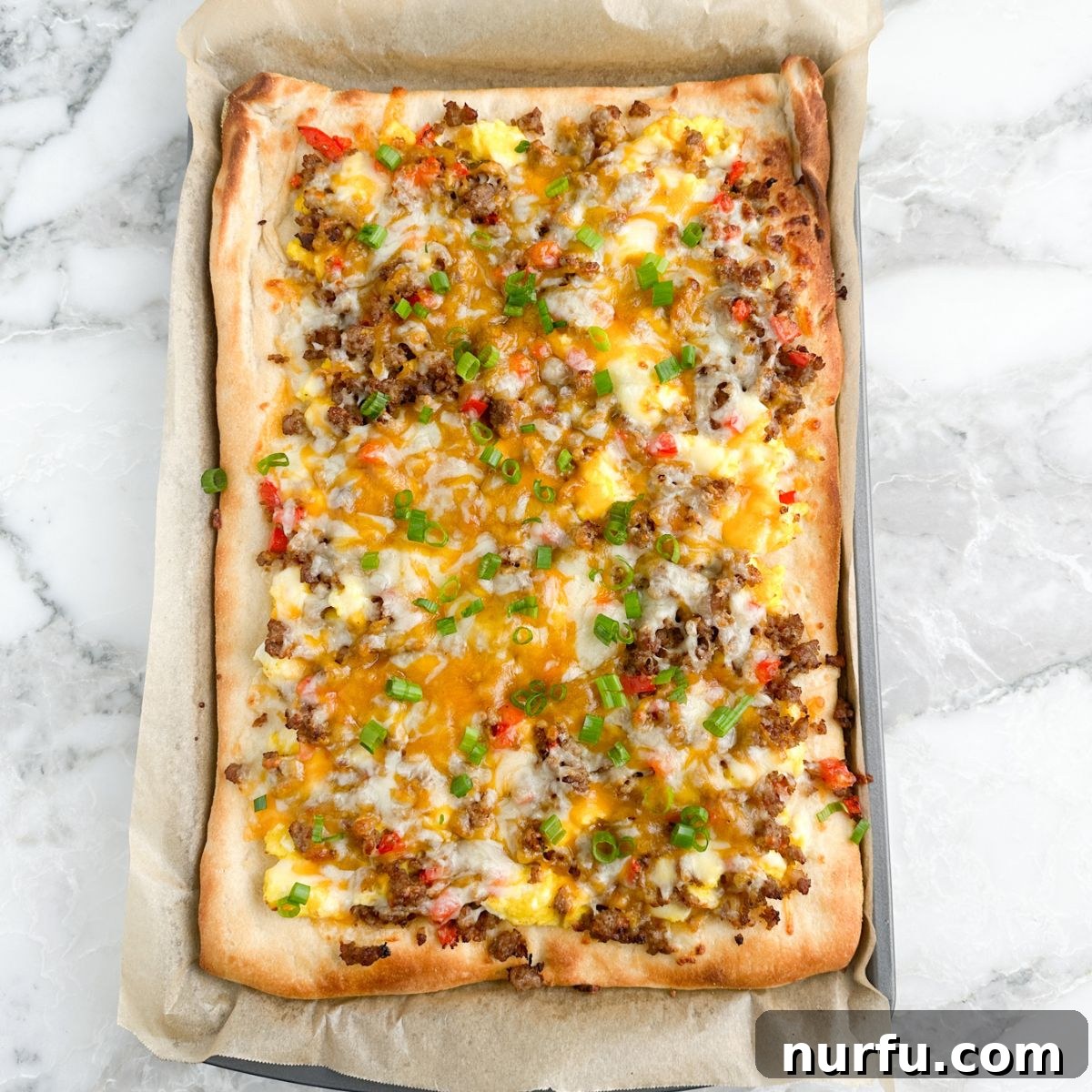 A large, rectangular breakfast pizza with varied toppings, served in a metal baking pan, ready to be sliced.
