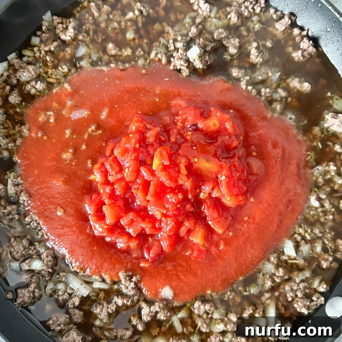 Hearty Slumgullion America's Beloved Goulash 5 Ground beef and tomato sauce mixture simmering in a skillet, infused with seasonings and beef broth, ready for the pasta.