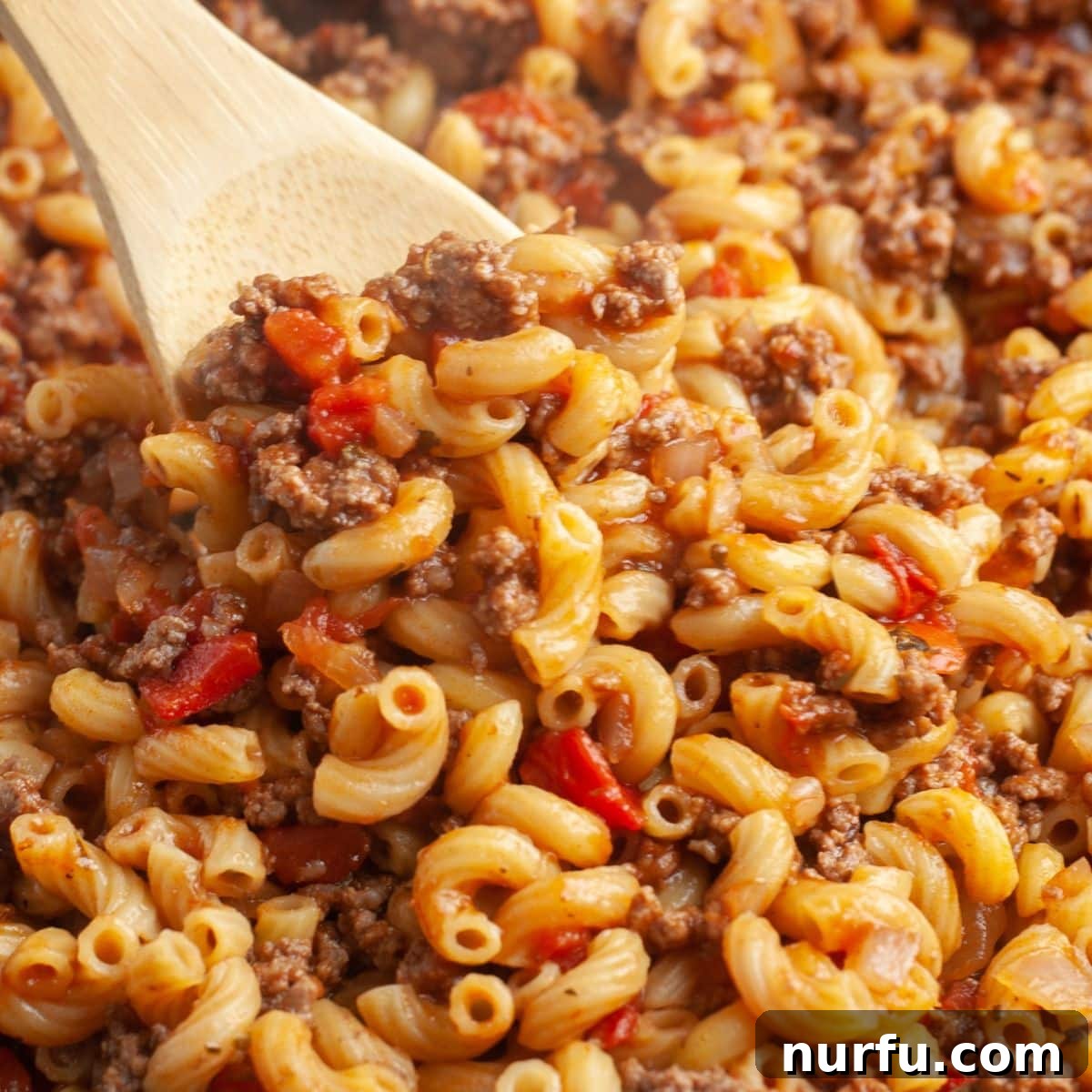 Hearty Slumgullion America's Beloved Goulash 6 Wooden spoon scooping a generous portion of beefy elbow macaroni from a skillet, showcasing the rich, hearty texture of Slumgullion.