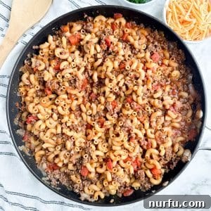 Skillet with ground beef, tomatoes, and macaroni, showing a completed Slumgullion dish ready for serving.