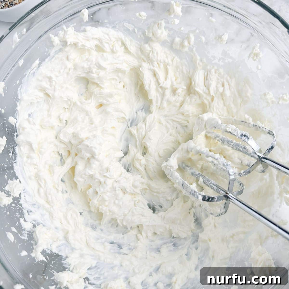 Quick & Creamy Bagel Dip 4 Whipped cream cheese and sour cream mixture in a bowl with an electric mixer, showing a smooth texture.