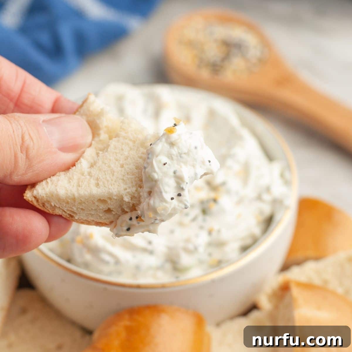 Quick & Creamy Bagel Dip 7 A hand dipping a piece of bagel into a bowl of creamy everything bagel dip.