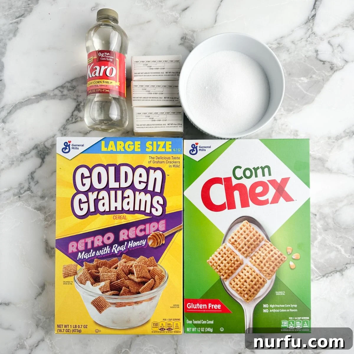 Individual ingredients for Sweet Chex Mix laid out: a bottle of light corn syrup, sticks of butter, a bowl of granulated sugar, a box of Golden Grahams cereal, and a box of Corn Chex cereal. All are neatly arranged on a white background, ready for mixing.