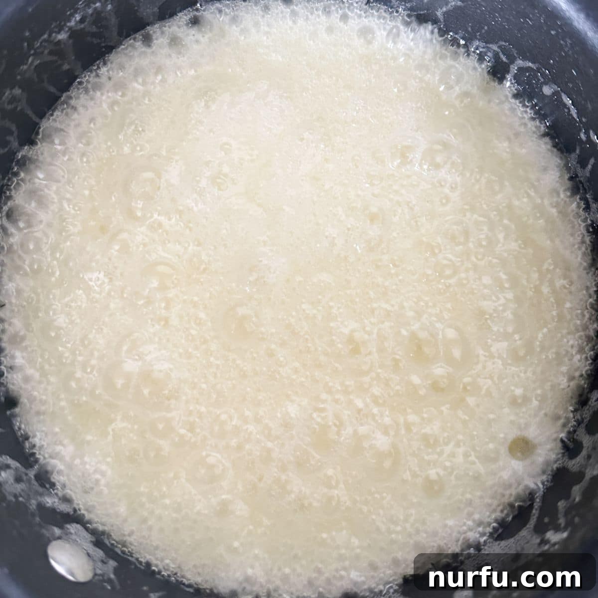A saucepan on a stovetop, containing the boiled corn syrup, butter, and sugar mixture, showing a light caramel color and ready to be poured over the cereal.