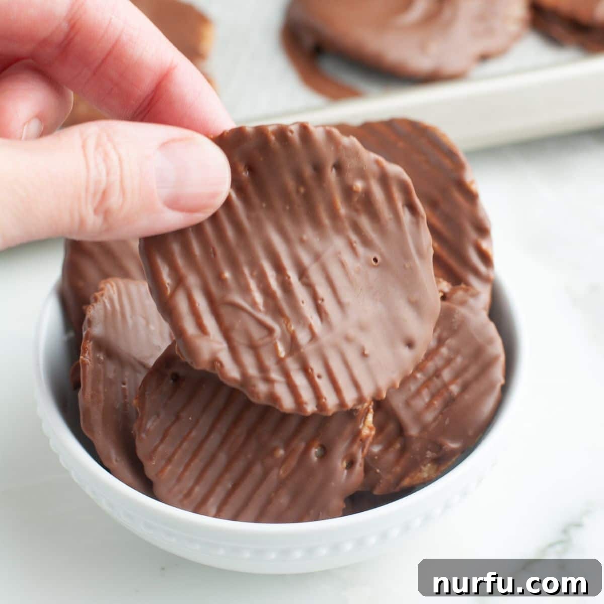 Sweet Salty Chocolate Chip Perfection 6 A hand delicately holding a single, perfectly coated chocolate covered potato chip, ready to be enjoyed.