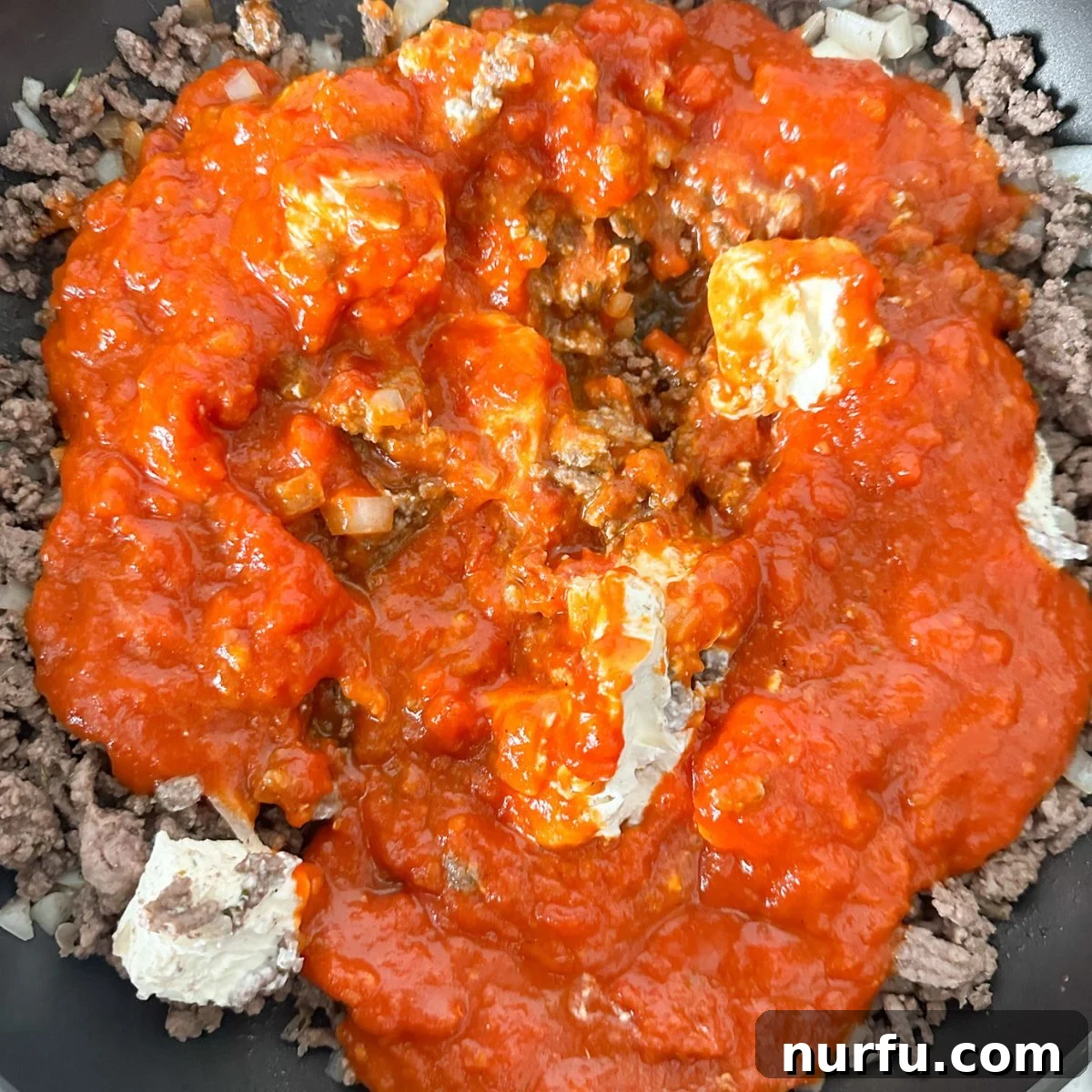 Golden Baked Tortellini 4 A skillet filled with rich, creamy meat sauce made from browned ground beef, melted cream cheese, and marinara sauce, simmering gently on the stove.