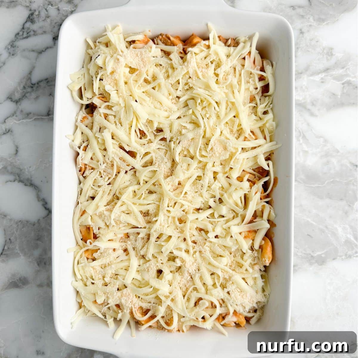 Golden Baked Tortellini 6 A casserole dish abundantly topped with shredded mozzarella and grated parmesan cheese, forming a delicious blanket over the tortellini and meat sauce, ready for baking.
