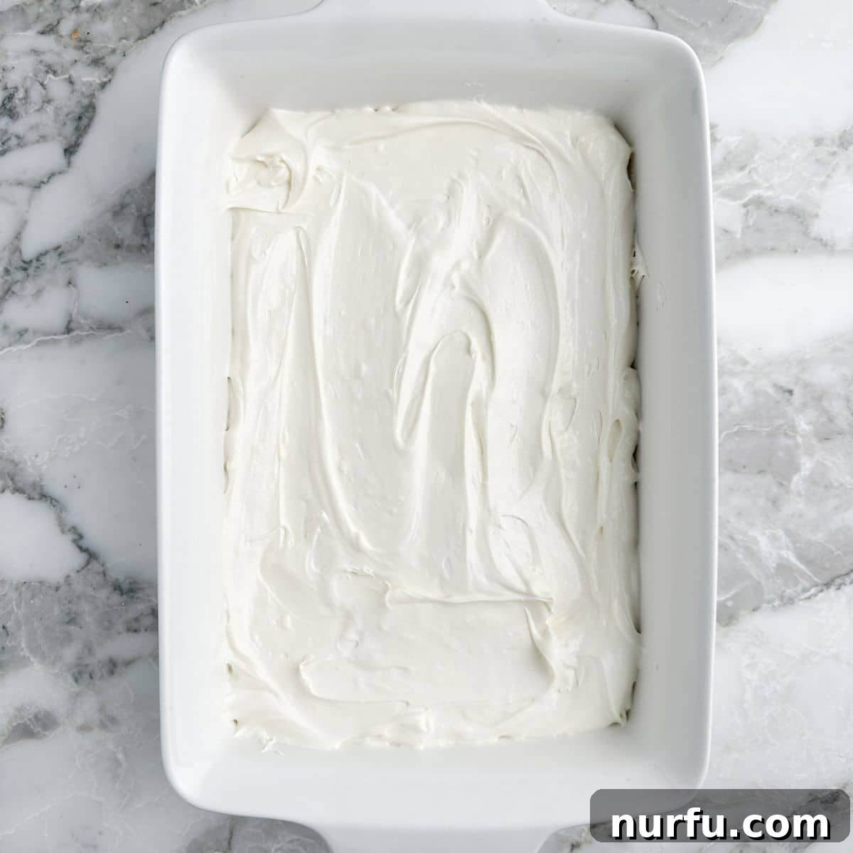 A 9x13 casserole dish with a smooth, white creamy spread forming the base layer of the dessert.