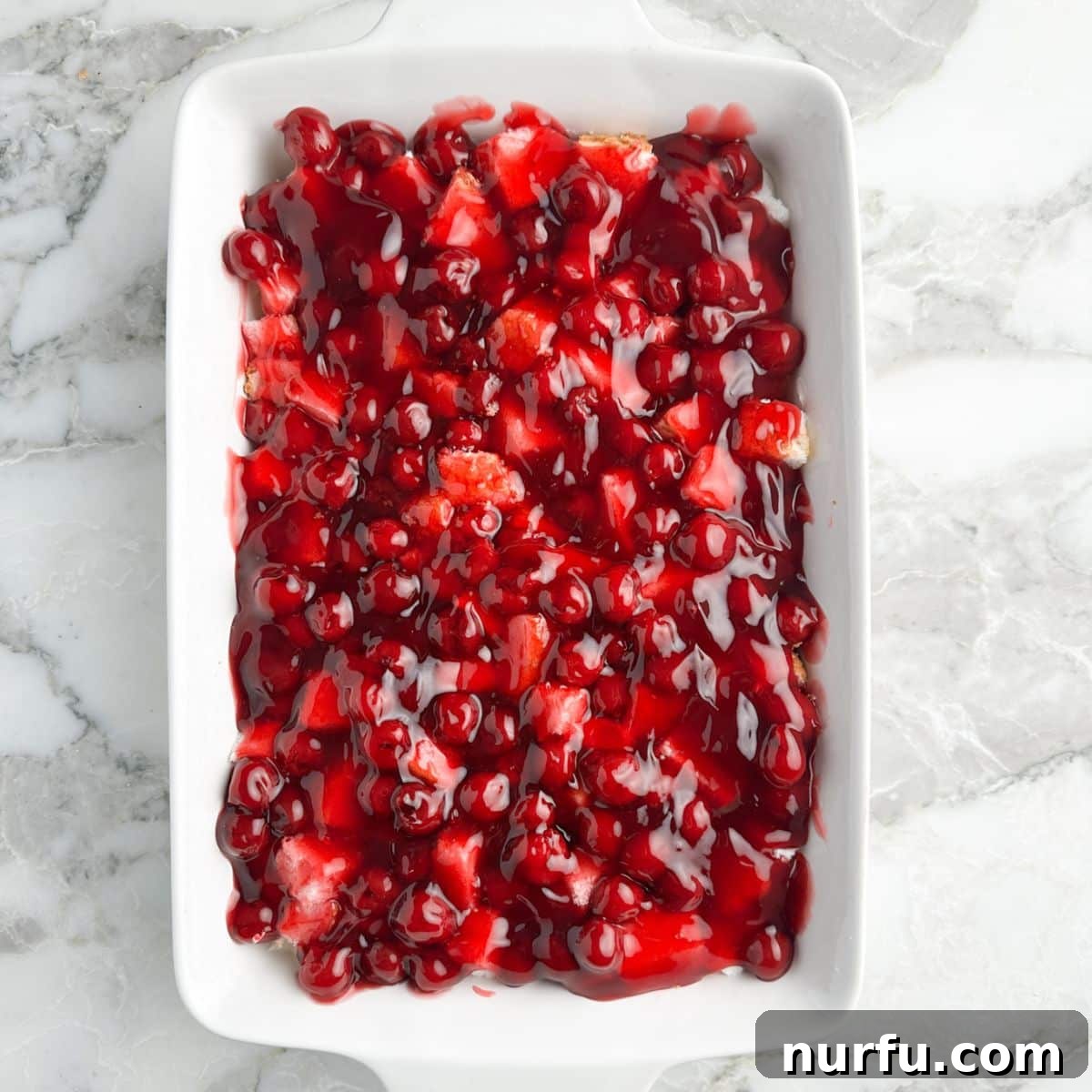 A 9x13 baking dish generously covered with vibrant cherry pie filling over the prepared layers, making a beautiful no-bake dessert.