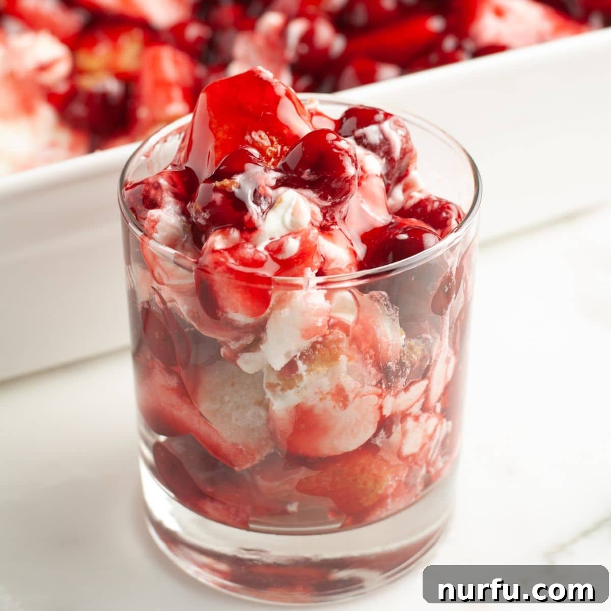 A perfectly cut slice of Cherries in the Snow dessert, revealing its distinct layers of angel food cake, creamy white base, and bright red cherry topping.