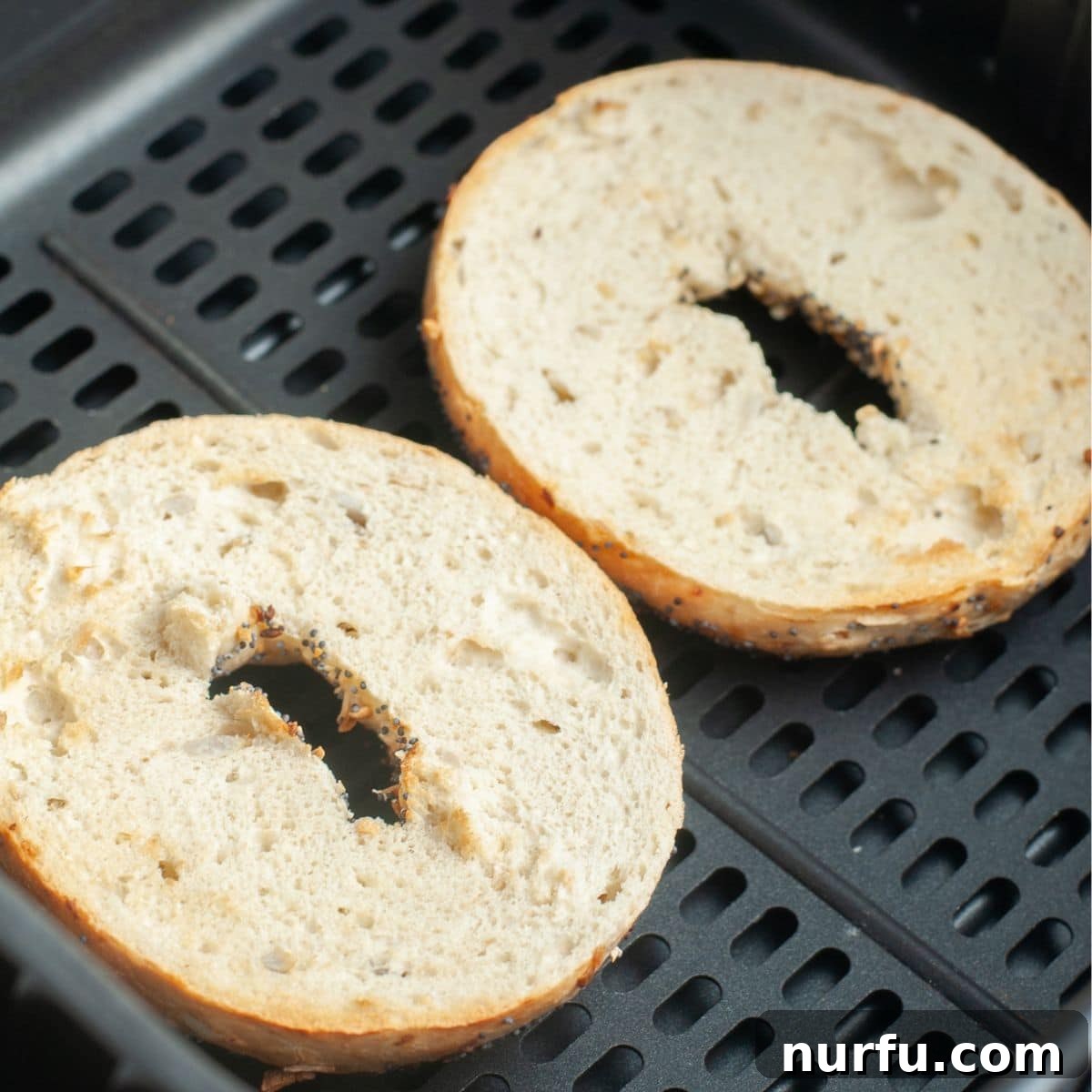 Air Fryer Bagels Crispy And Quick 3 Two bagel halves, cut side up, neatly arranged in the basket of an air fryer, ready for toasting. The basket is clean and spacious.