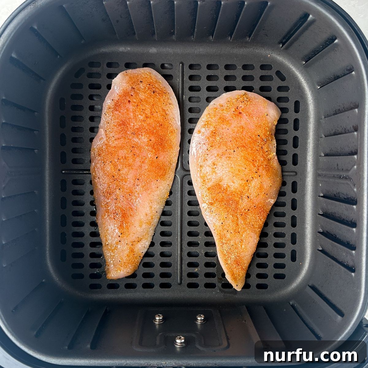 Quick Air Fryer Thin Chicken Breasts 4 Seasoned thin chicken breasts arranged in a single layer inside an air fryer basket, ready for cooking.
