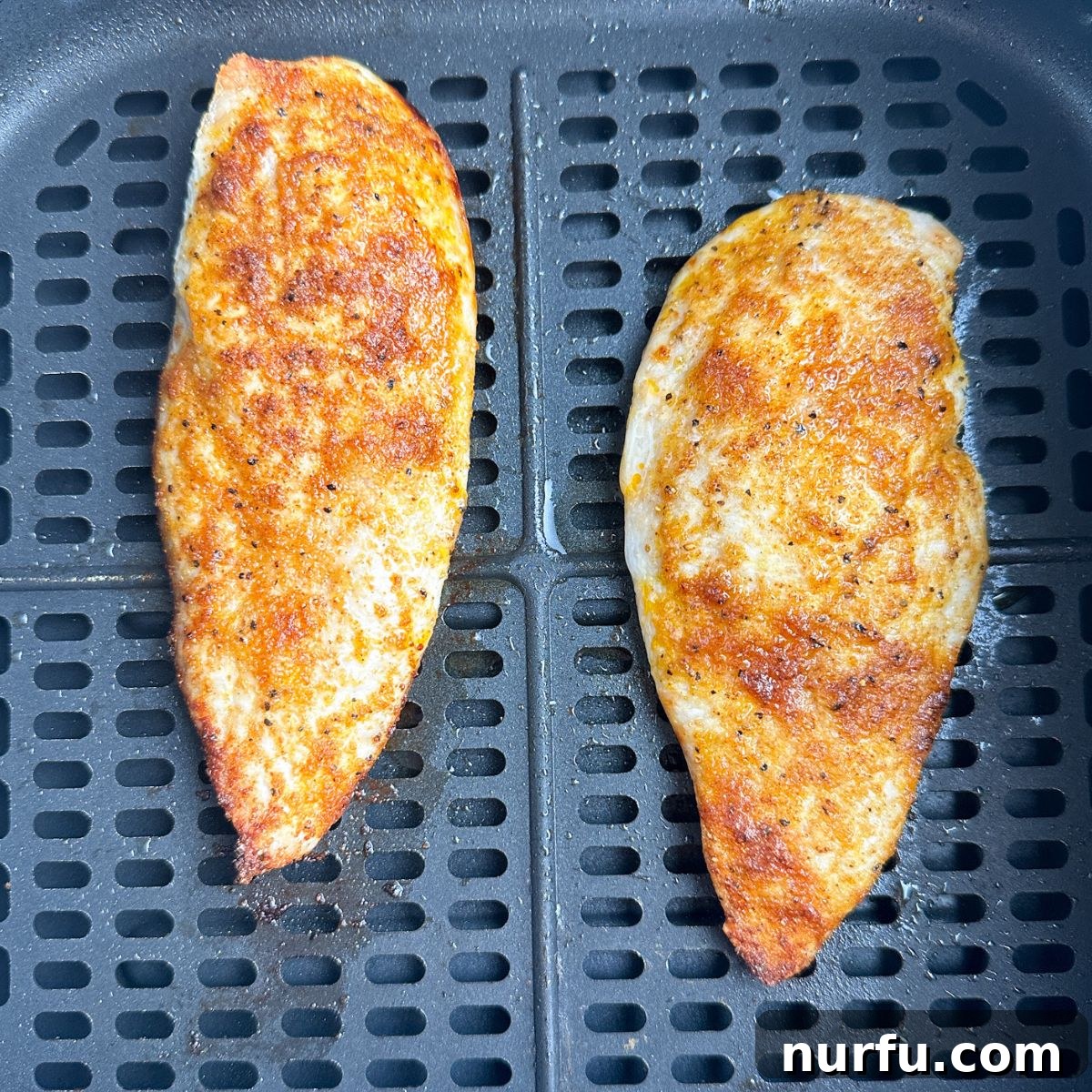 Quick Air Fryer Thin Chicken Breasts 5 Two perfectly cooked, golden-brown thin chicken breasts resting in an air fryer basket after cooking.