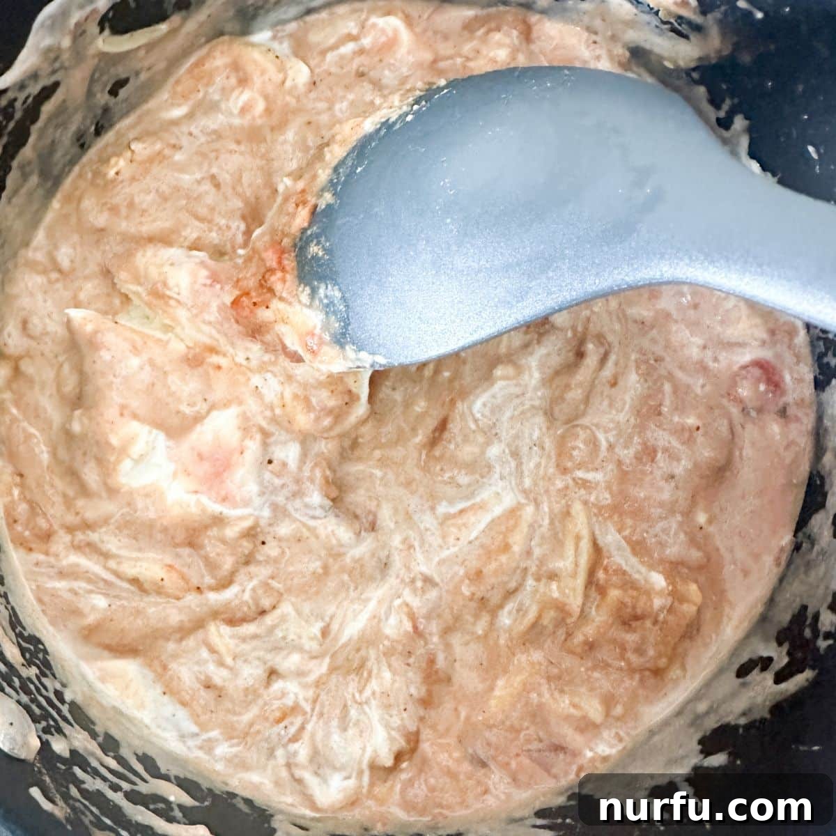 Creamy Fiesta Bean Dip 5 A close-up shot of the refried bean dip mixture in a saucepan, being actively stirred with a spoon. The ingredients have started to combine, showing a creamy, light brown texture with melted cheese.