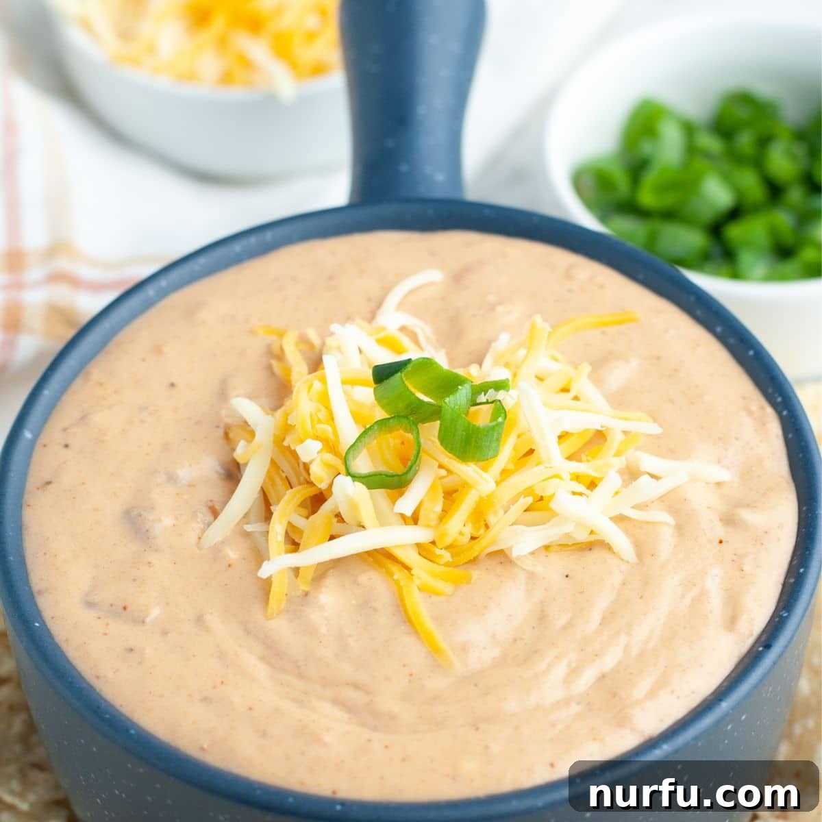 Creamy Fiesta Bean Dip 6 A beautifully presented bowl of refried bean dip, generously topped with shredded cheese and bright green onions, ready to be served. The dip appears rich and inviting, with the vibrant garnishes creating an appealing contrast.