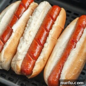 Perfect Air Fryer Hot Dogs 8 Hot dogs in buns in an air fryer basket.