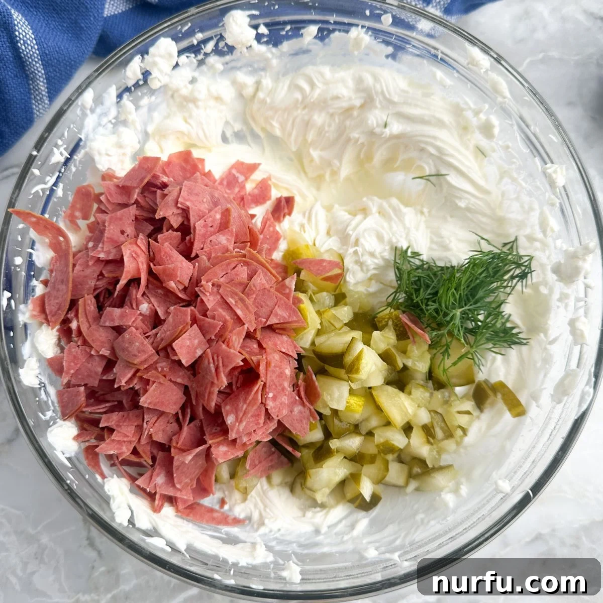 Zesty Dill Pickle & Dried Beef Dip 5 A mixing bowl filled with the creamy base, now containing chopped dried beef and diced dill pickles, being stirred to combine.