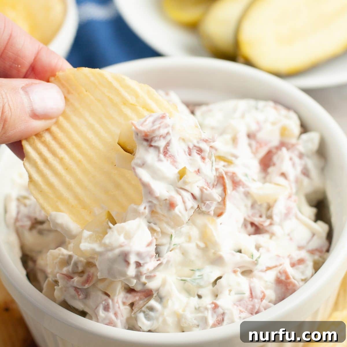 Zesty Dill Pickle & Dried Beef Dip 6 A single potato chip generously loaded with creamy dill pickle dip, showcasing its irresistible texture.