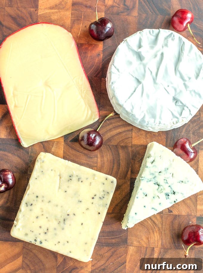 Four distinct cheeses, including Brie, blue cheese, cheddar, and Gouda, arranged on a rustic cutting board with fresh cherries.