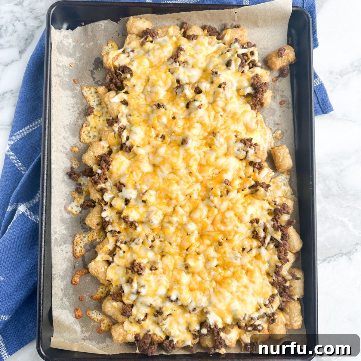 Ultimate Beef Tater Tot Nachos 4 A baking sheet filled with golden tater tots, topped with seasoned ground beef and a generous layer of melted cheese, just out of the oven.