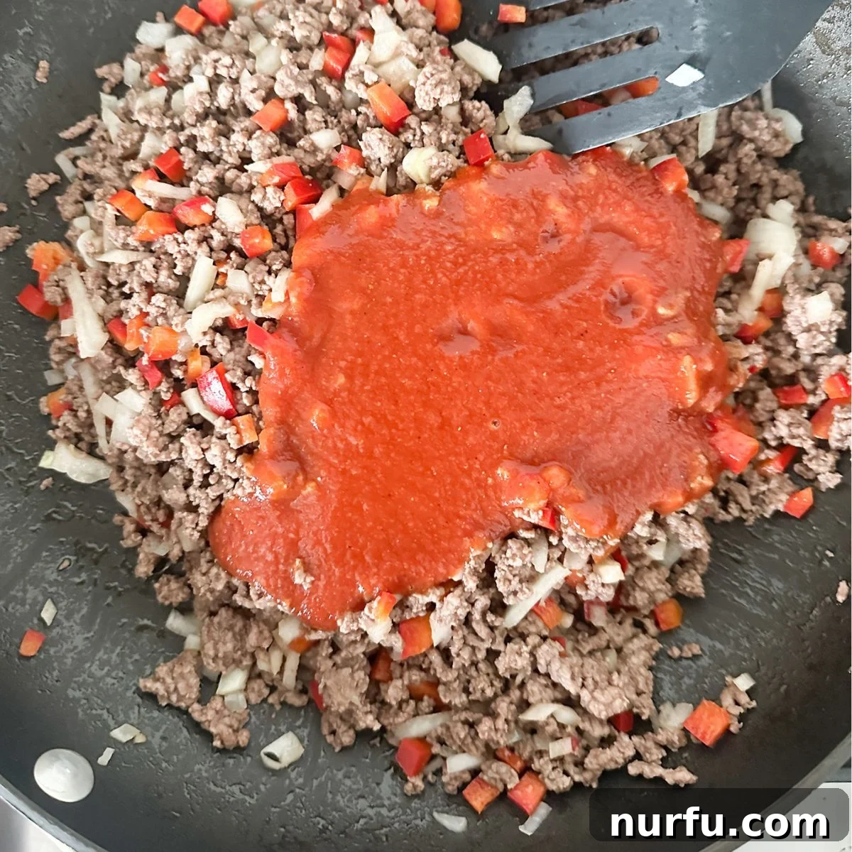 A large skillet filled with browned ground beef, diced onions, bell peppers, and rich sloppy joe sauce, simmering gently.