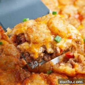 A spatula lifting a portion of Sloppy Joe Tater Tot Casserole from a baking dish, showing the layers of meat, cheese, and crispy tots.
