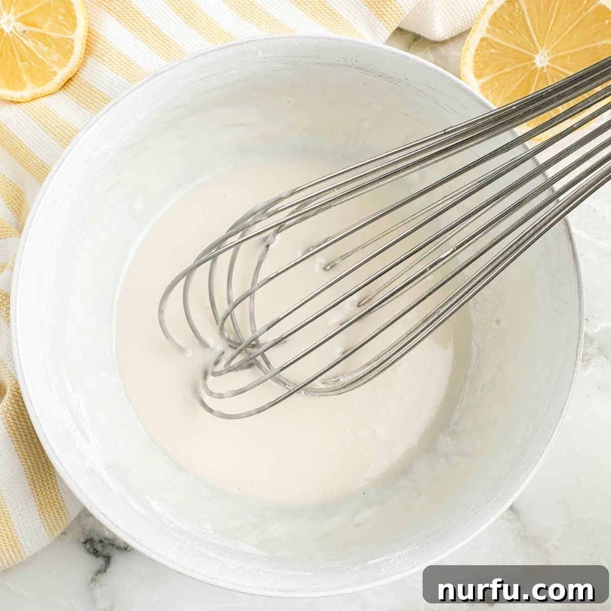 A bowl of freshly made lemon glaze, perfectly whisked and ready to use, with a whisk resting in it.