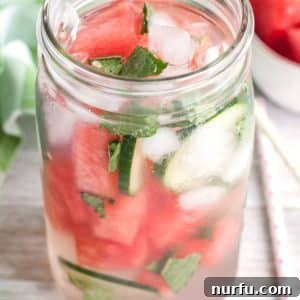 A glass of water with watermelon, cucumber, and mint.