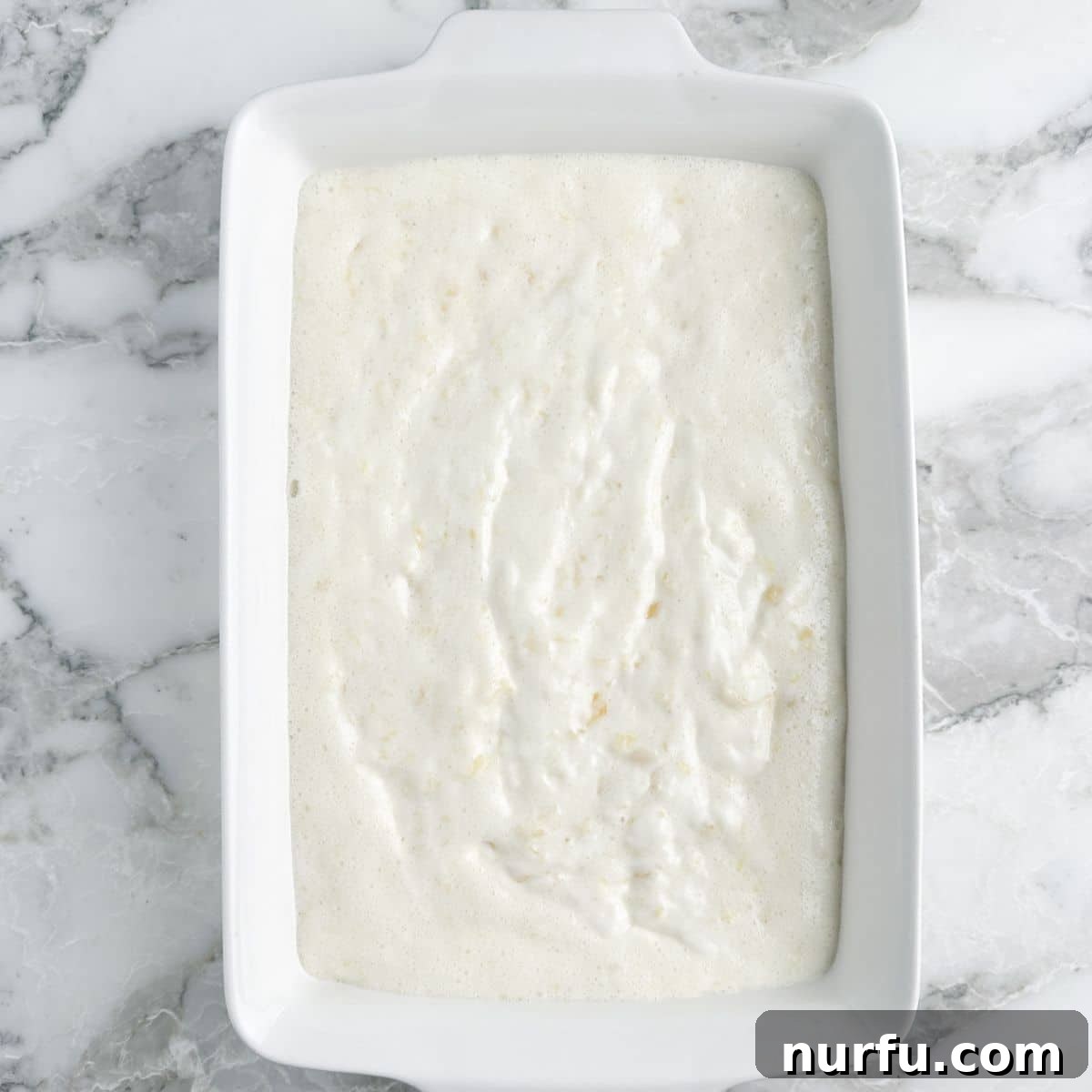 A 9x13 inch baking dish is filled with the airy angel food cake batter mixed with crushed pineapple, ready to be baked into a golden-brown dessert.