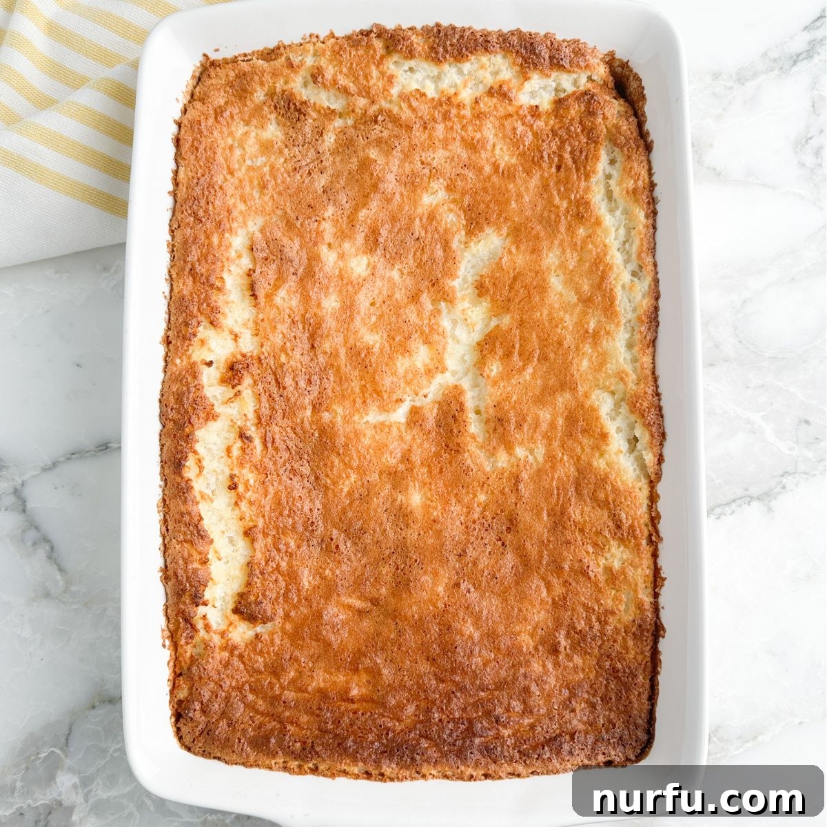 A delicious angel food cake, baked to a golden brown, cooling in a 9x13 inch baking dish, ready to be topped and served.