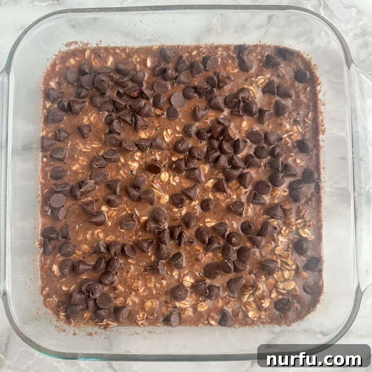 Decadent Chocolate Baked Oats 5 Baked oatmeal with chocolate chips ready for baking in a glass baking dish.