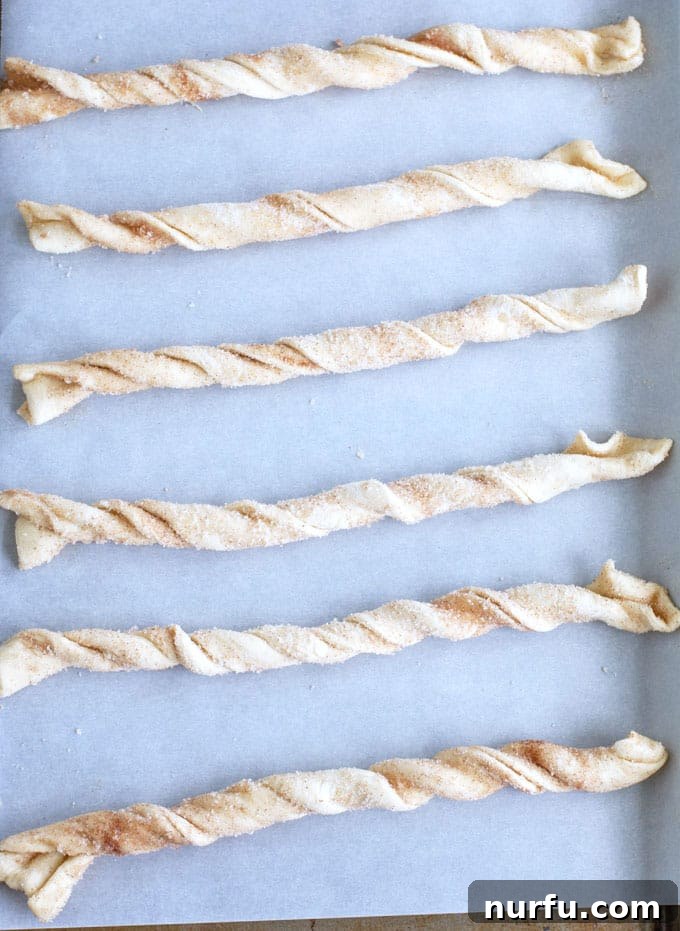Freshly baked cinnamon twists cooling on a parchment-lined baking sheet, showcasing their golden-brown color and flaky texture.