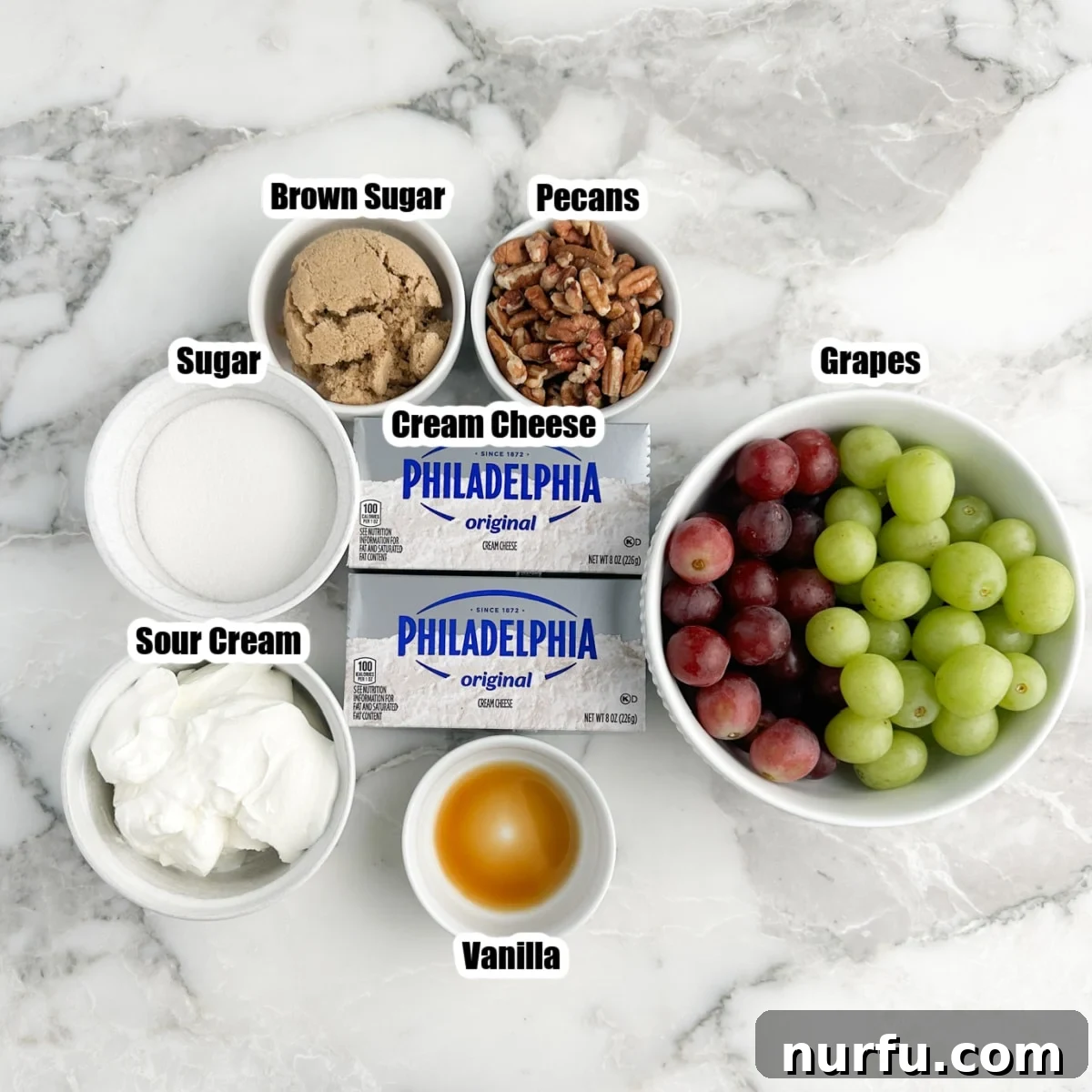 Homestyle Chicken Salad Chick Grape Salad 3 A flat lay photograph showcasing all the primary ingredients required for the grape salad: a brick of cream cheese, a large bowl of fresh grapes, a bag of granulated sugar, a tub of sour cream, a bag of light brown sugar, and a bowl of chopped pecans.