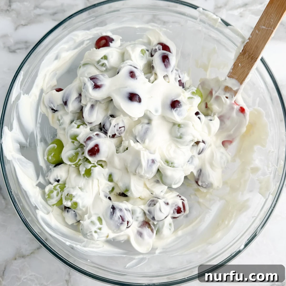 Homestyle Chicken Salad Chick Grape Salad 4 A large glass bowl filled with vibrant green and red grapes, completely coated in a rich, white, creamy dressing, ready for chilling.