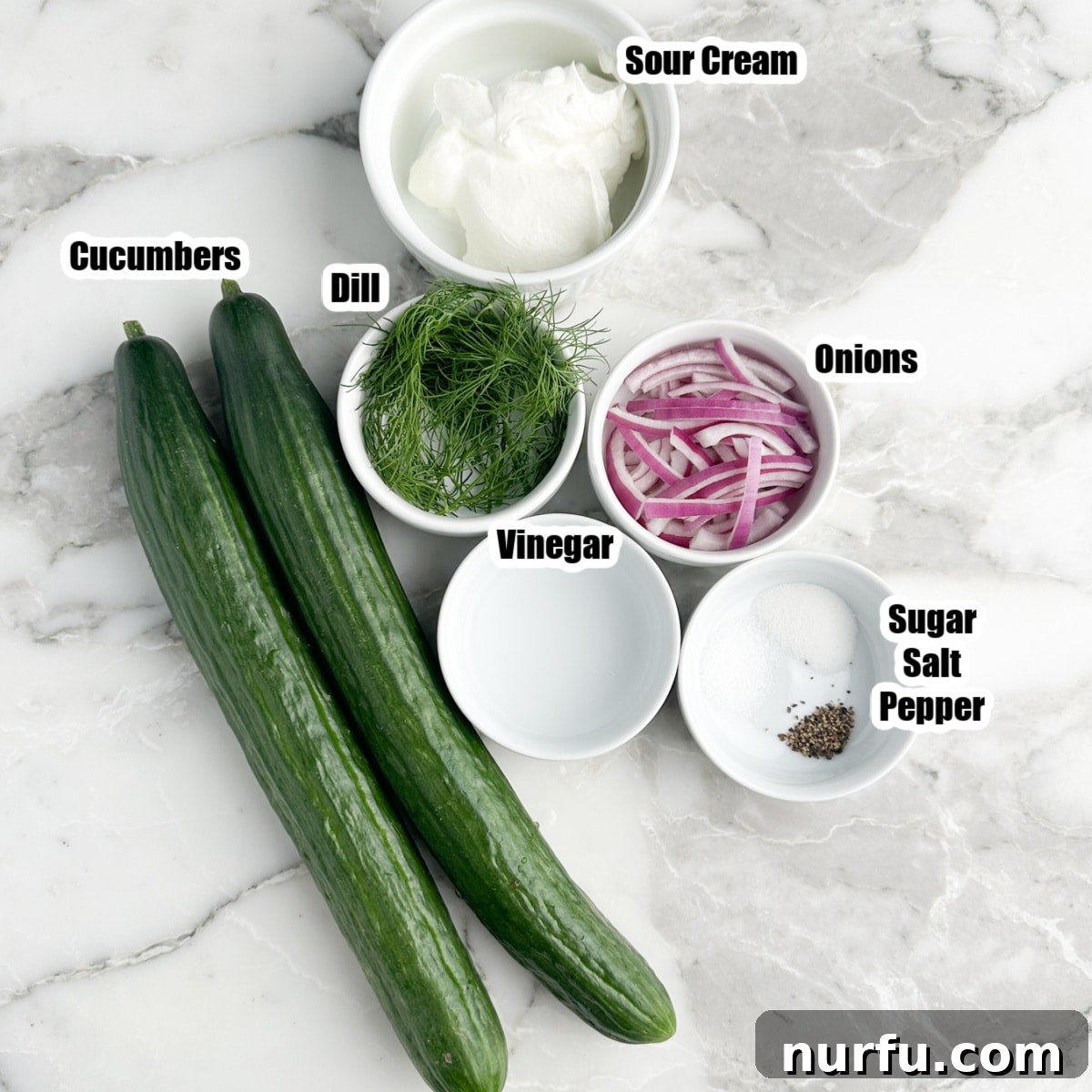 Refreshing Creamy Cucumber Dill Salad 3 Arrangement of fresh ingredients for cucumber dill salad: two whole cucumbers, a bowl of sour cream, fresh dill sprigs, sliced red onions, a bottle of vinegar, and small bowls of salt, pepper, and sugar.