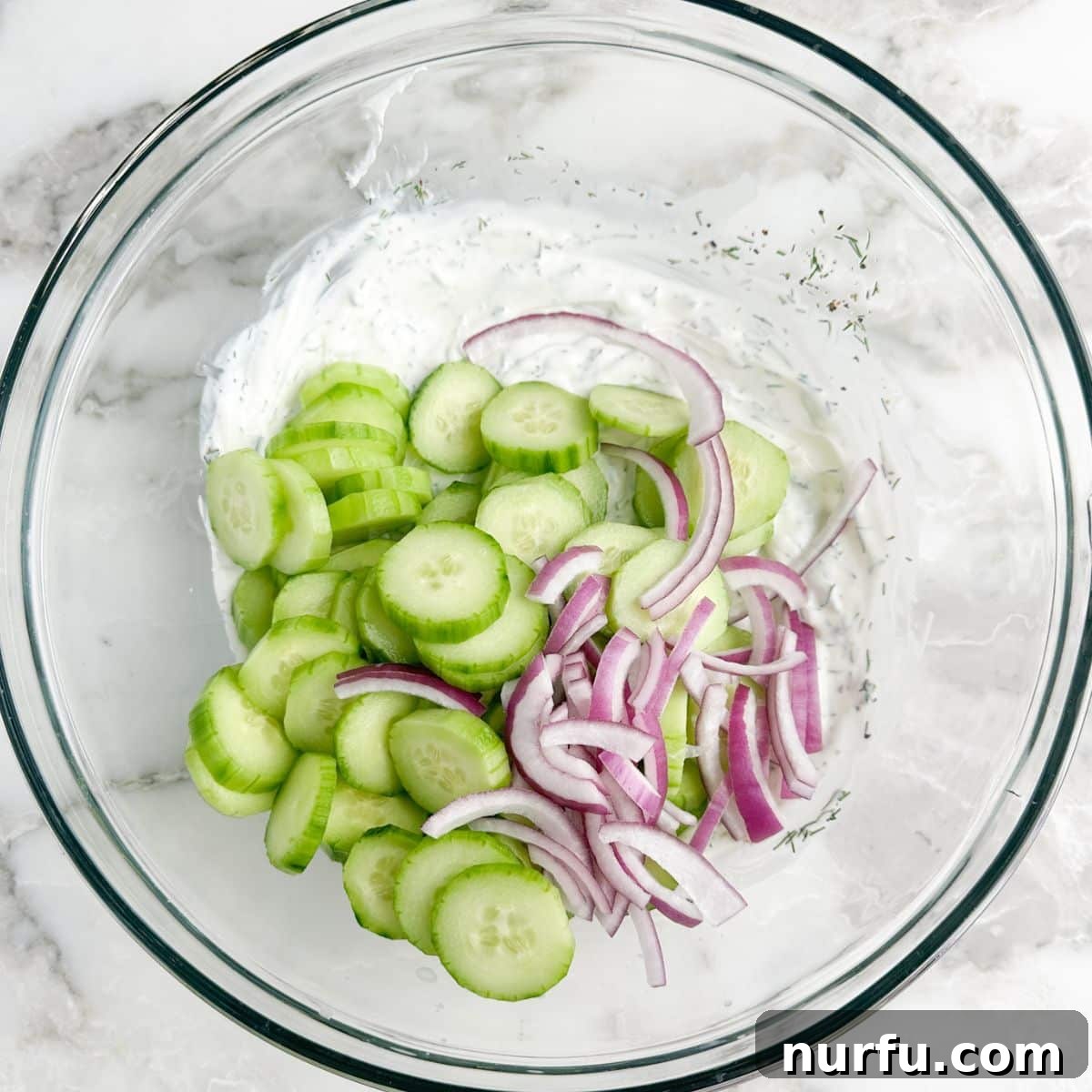 Refreshing Creamy Cucumber Dill Salad 5 A large bowl filled with creamy dressing, mixed with thin slices of cucumber and red onion, tossed and ready.
