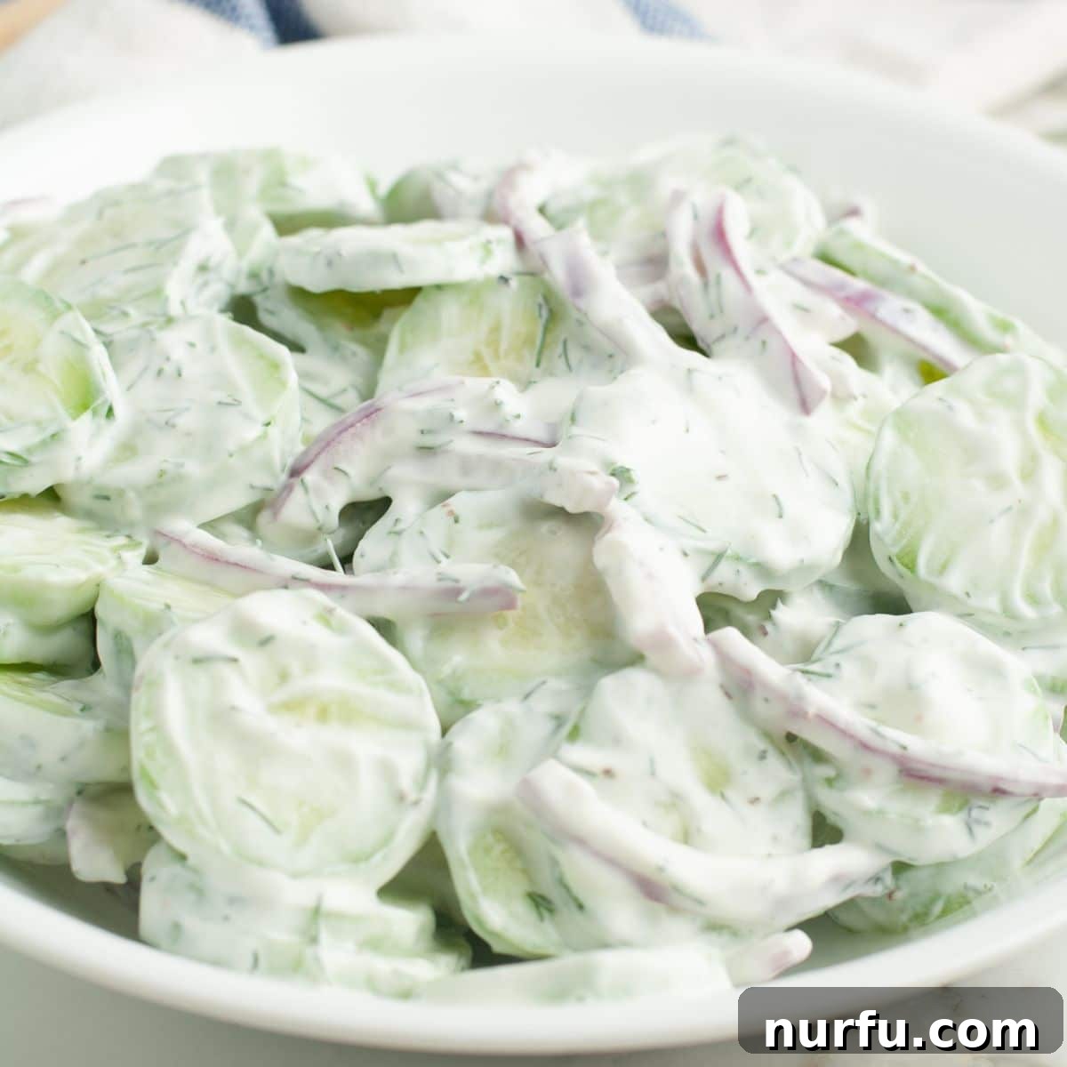 Refreshing Creamy Cucumber Dill Salad 6 A bowl of creamy cucumber and red onion salad, garnished with fresh dill sprigs, ready to be served.