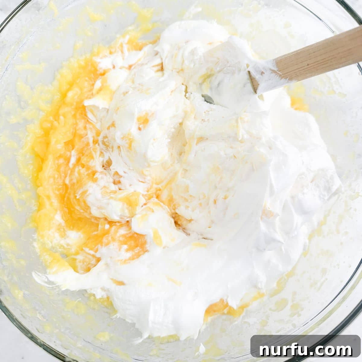 Bowl of Cool Whip and crushed pineapple mixture, showing a creamy texture before chilling.