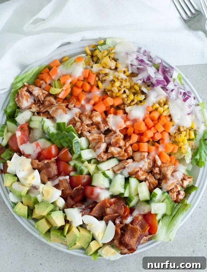 Smoky BBQ Chicken Cobb Salad 2 A vibrant BBQ Chicken Cobb Salad featuring grilled chicken, hard-boiled eggs, crispy bacon, roasted corn, fresh tomatoes, avocado slices, and green lettuce, all drizzled with dressing.