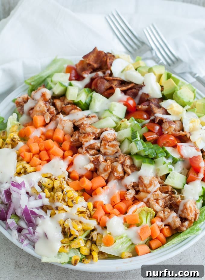 Smoky BBQ Chicken Cobb Salad 4 Close-up of a portion of BBQ Chicken Cobb Salad in a bowl, showing the rich textures of roasted corn, diced avocado, and seasoned chicken amongst fresh greens.