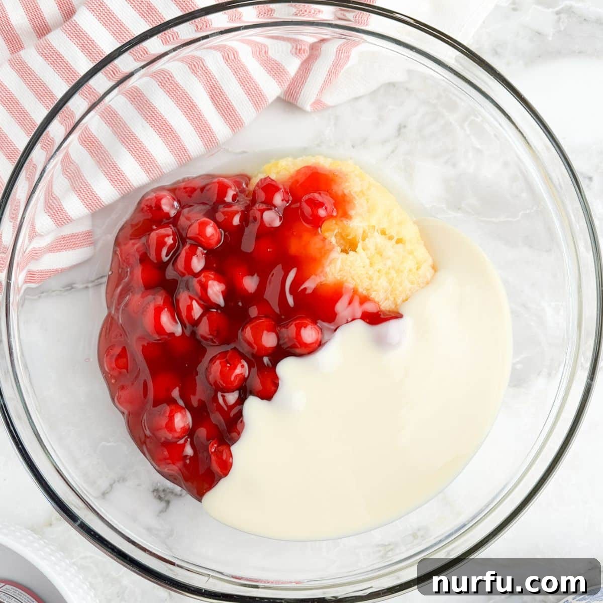 A bowl containing cherry pie filling, crushed pineapple, and sweetened condensed milk, mixed together.