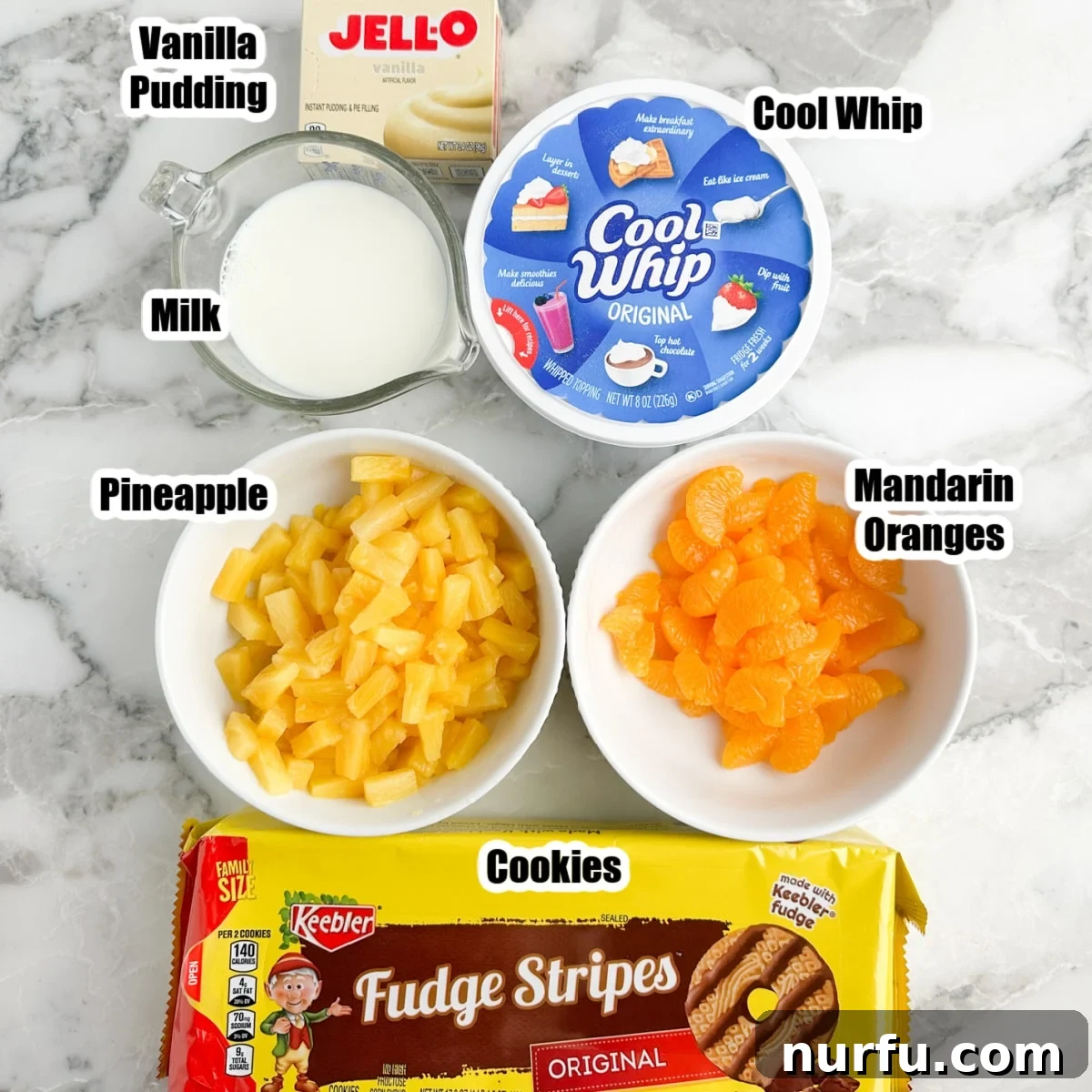 The Ultimate Cookie Salad 3 Individual ingredients for cookie salad laid out: vanilla pudding mix, milk, Cool Whip, canned pineapple, mandarin oranges, and a stack of Fudge Striped cookies.