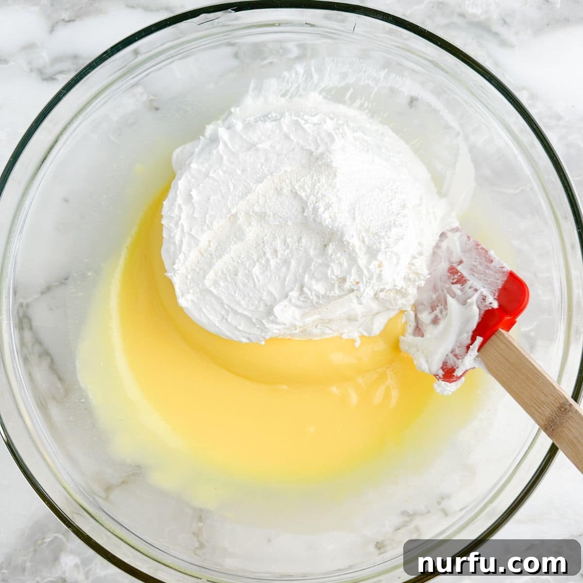 The Ultimate Cookie Salad 4 Bowl with vanilla pudding and Cool Whip being gently mixed.