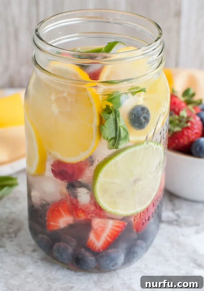 Mason jar glass filled with oranges, strawberries, blueberries, raspberries and fresh basil for Rainbow Detox Water
