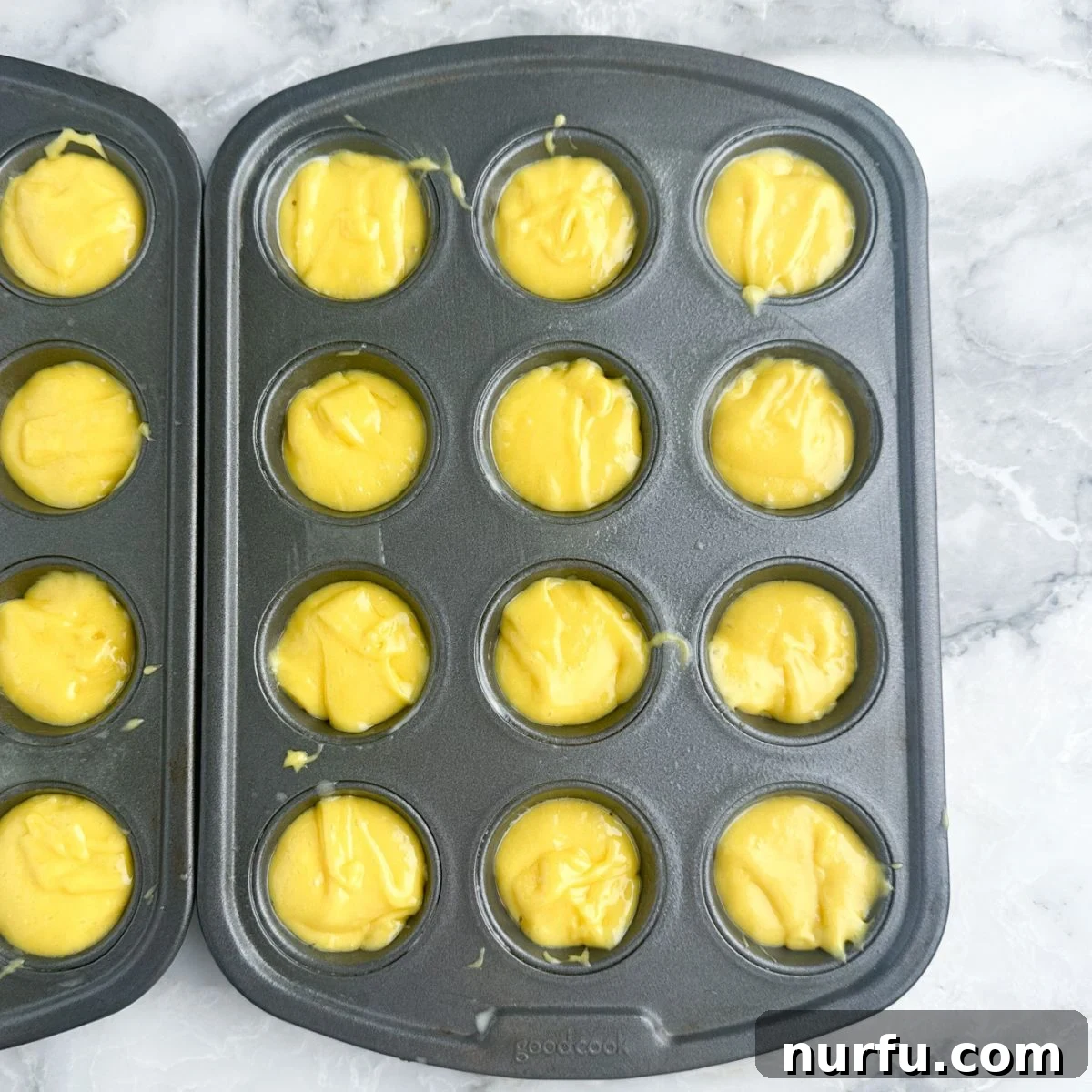 Close-up shot of vibrant yellow lemon cake batter expertly spooned into a mini muffin tin, ready for baking.