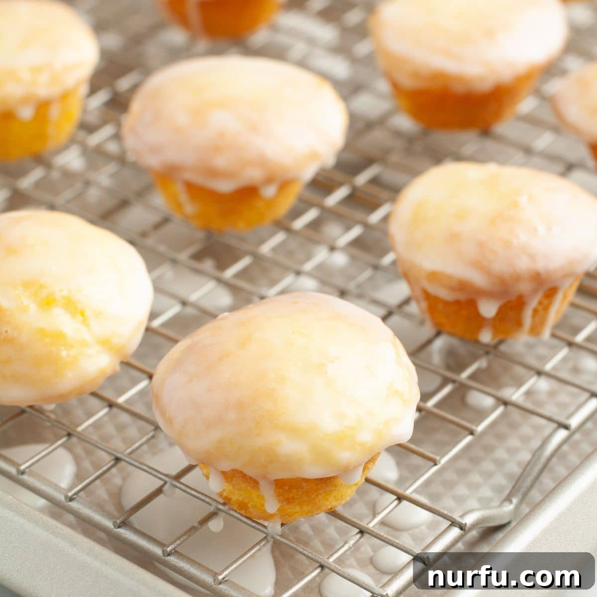 A close-up of several perfectly glazed lemon blossom bites arranged on a wire cooling rack, glistening under the light.