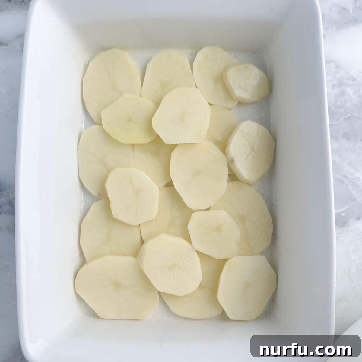 Creamy Stroganoff Potato Casserole 5 First layer of sliced potatoes in a casserole dish.