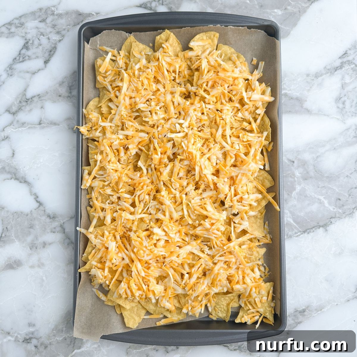 Mastering Guacamole Nachos 4 A baking sheet is perfectly lined with crispy tortilla chips, generously topped with a blanket of shredded cheese, ready for the oven to create gooey nachos.