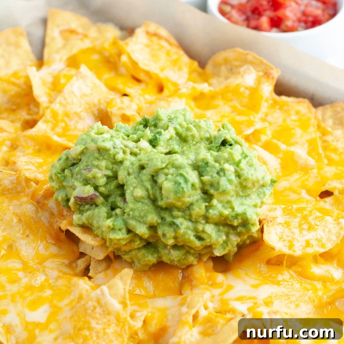 Mastering Guacamole Nachos 6 A tantalizing platter of freshly baked tortilla chips, generously topped with melted cheese and dollops of vibrant homemade guacamole, ready to be enjoyed.