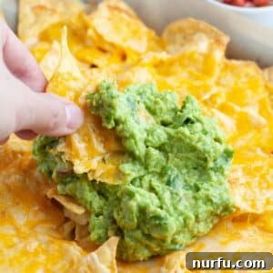 Hand holding nachos with guacamole.